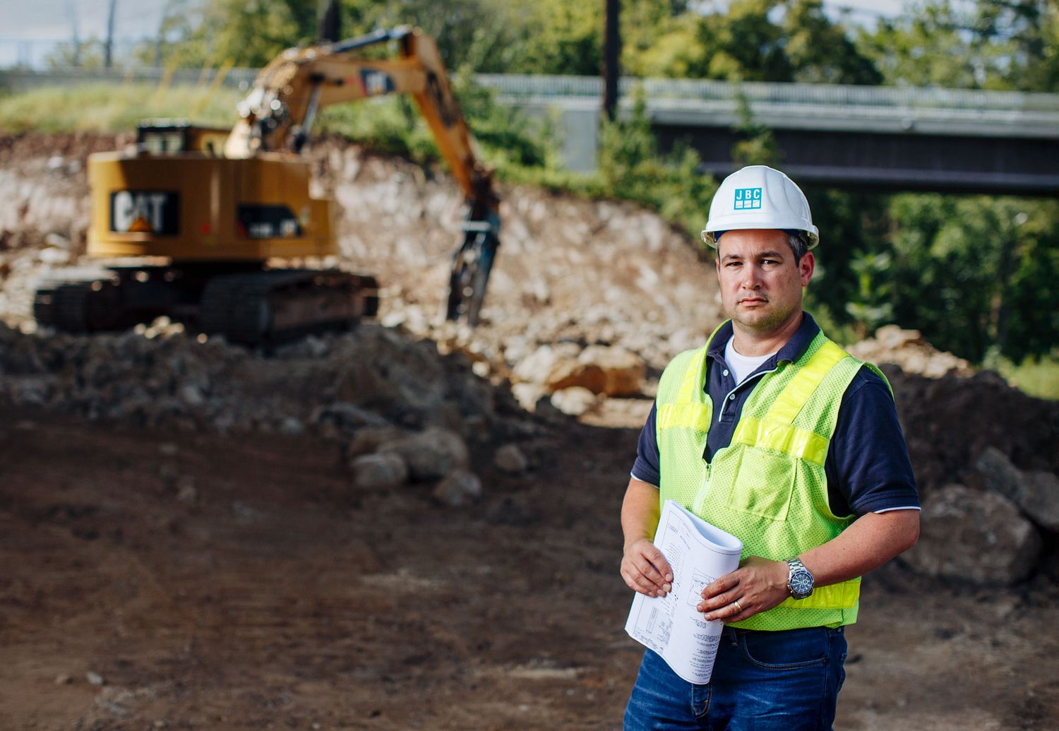 Construction project manager in safety vest and hard hat standing at an excavation site.