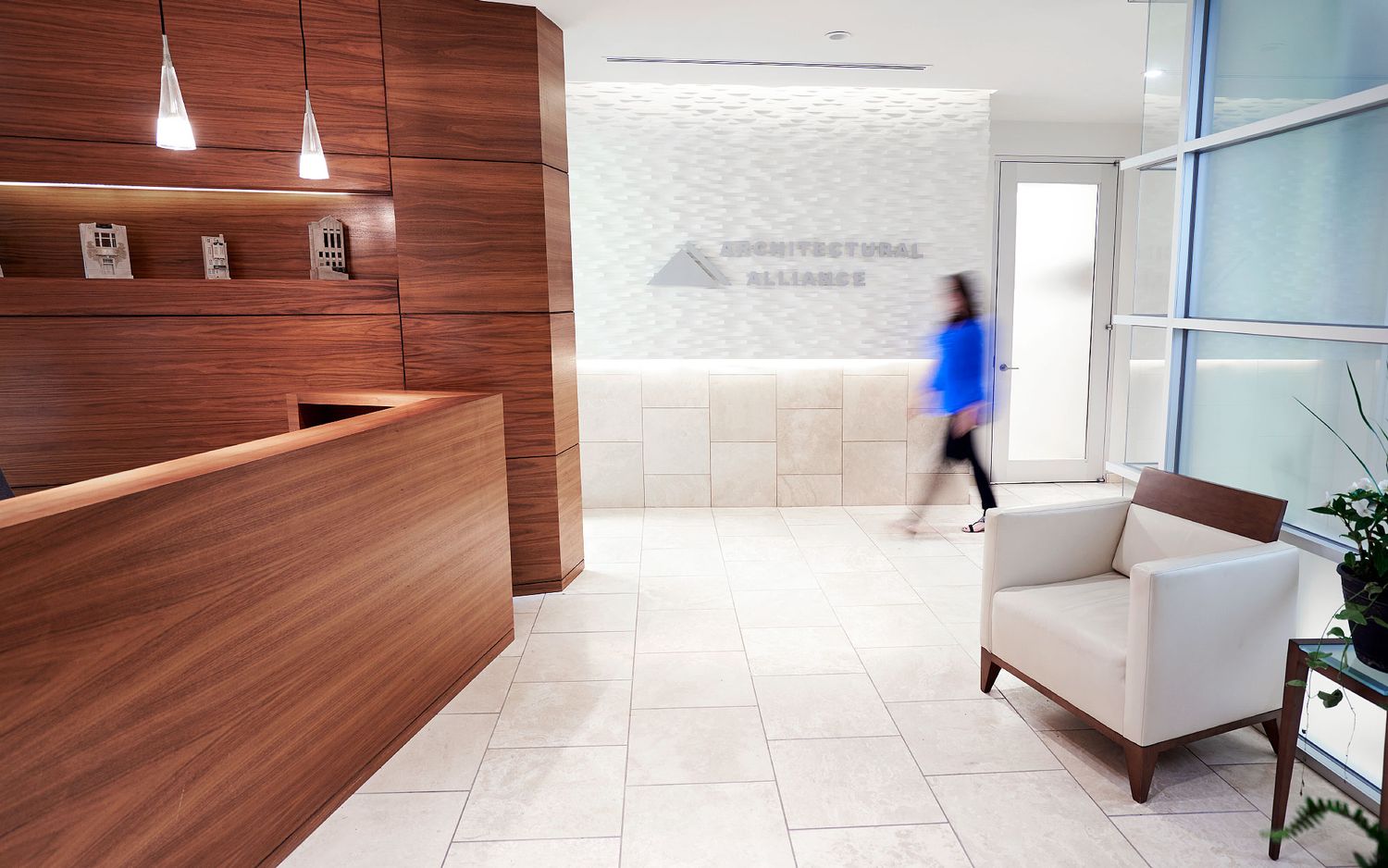 Modern corporate office reception area with wooden desk and illuminated company logo on white wall.