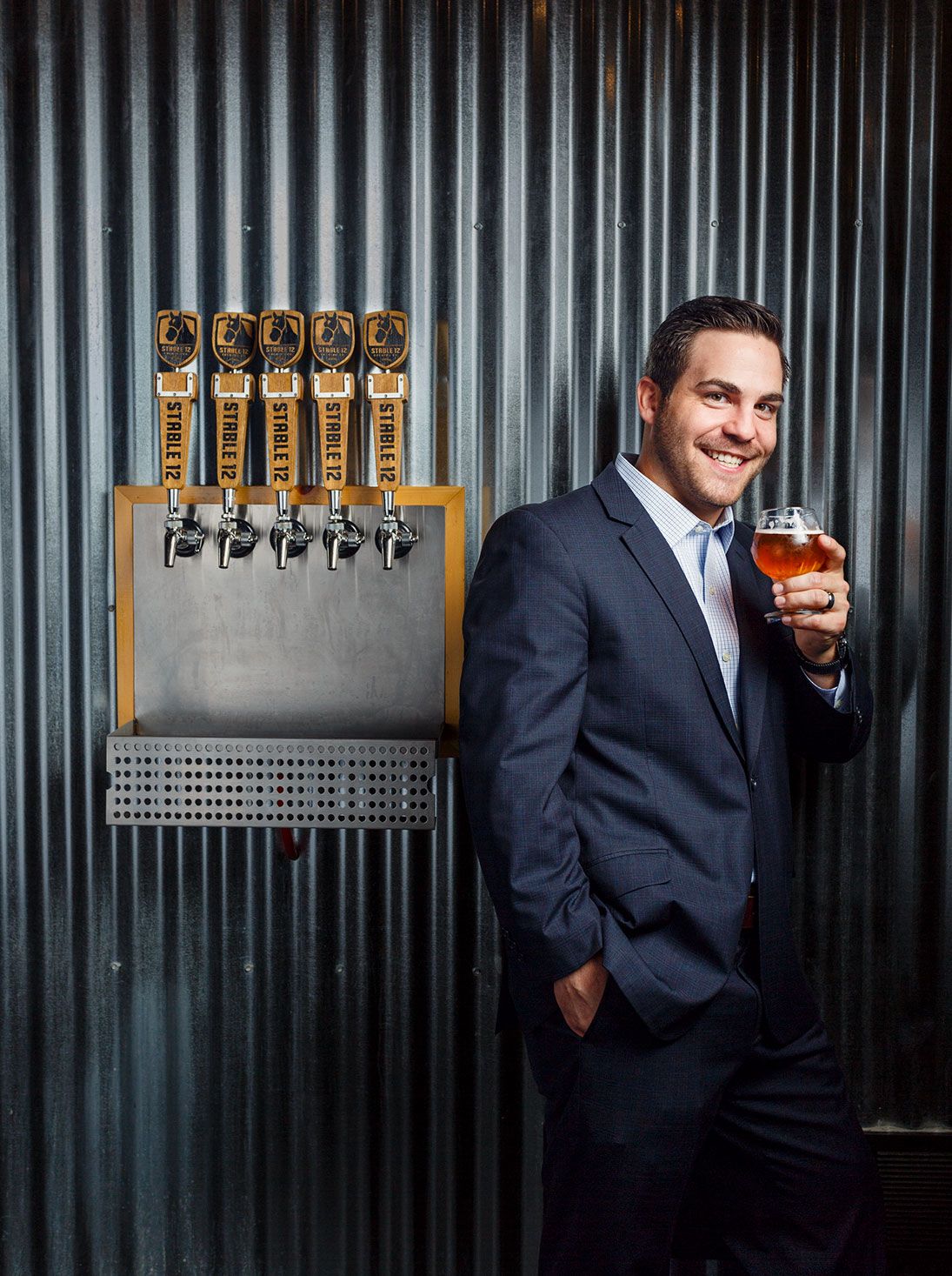 Man in suit holding craft beer glass beside tap handles at a brewery bar.
