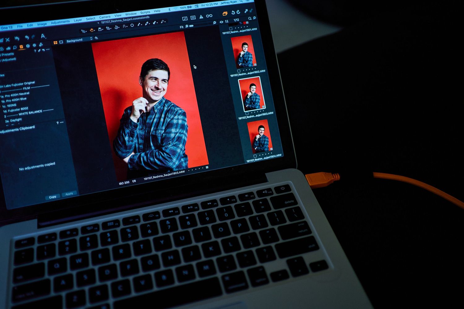 Laptop screen displaying photo editing software with a portrait of a man in a plaid shirt against a red background.