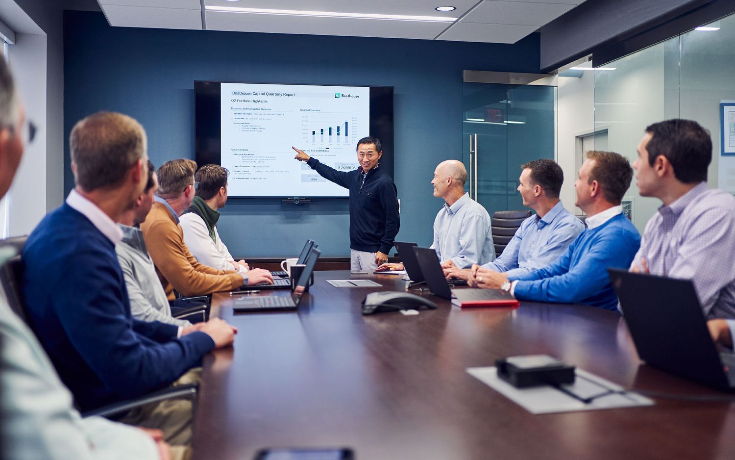 Business presenter pointing at data charts on a screen during a corporate boardroom meeting.
