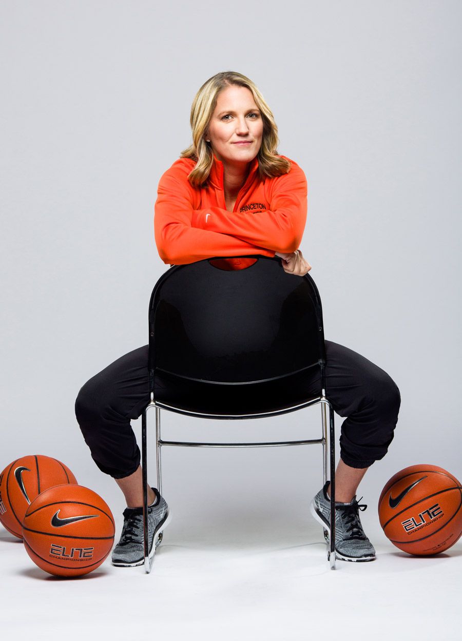Woman in orange jacket sitting on chair surrounded by Nike Elite basketballs in studio setting.