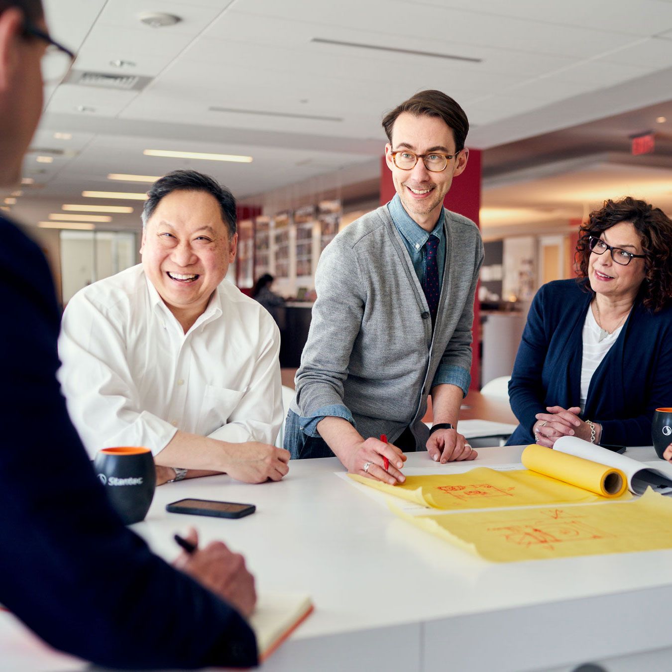 Diverse business team collaborating around a conference table with blueprints in a modern office setting.