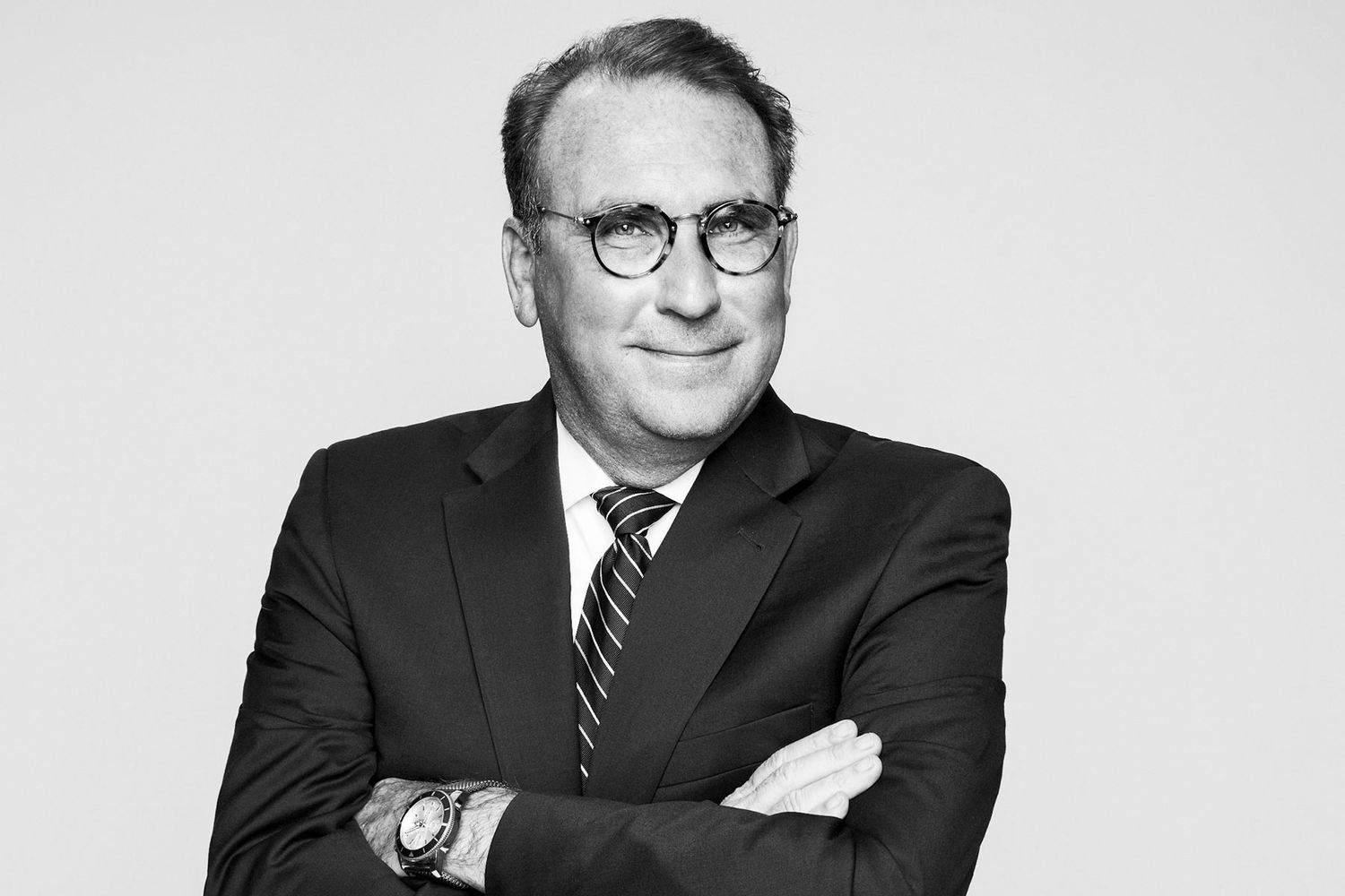 Black and white professional portrait of a senior businessman in a suit with arms crossed.