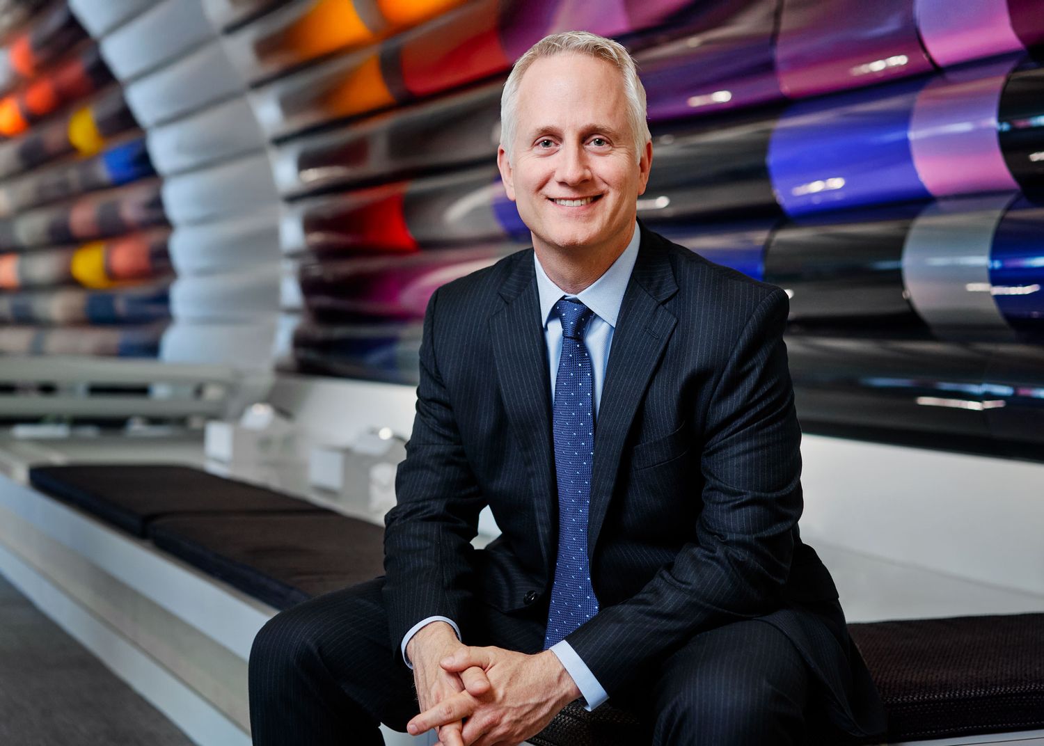 Smiling corporate executive in black suit poses in front of colorful cylindrical display wall.
