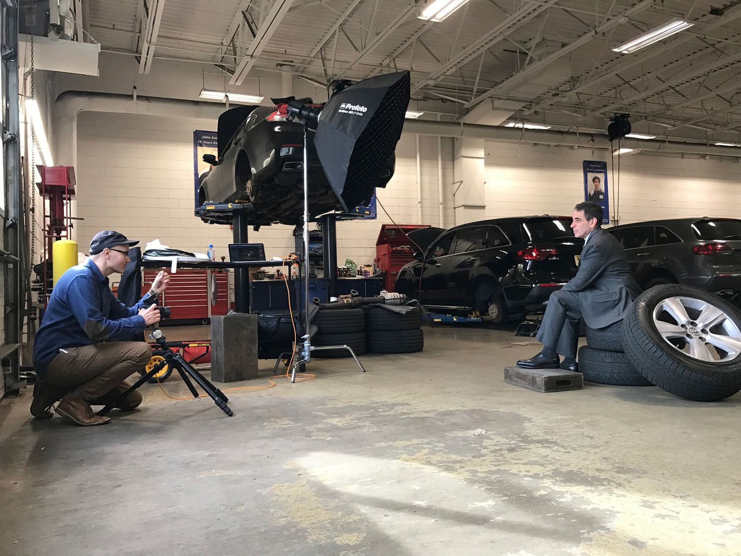 Film crew shooting an interview in an auto repair garage with professional lighting equipment and cameras.