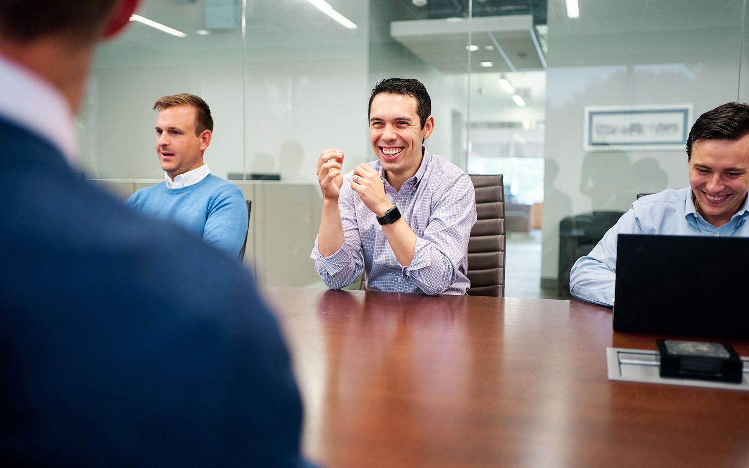 Three smiling businessmen engaged in a positive discussion during a corporate boardroom meeting.