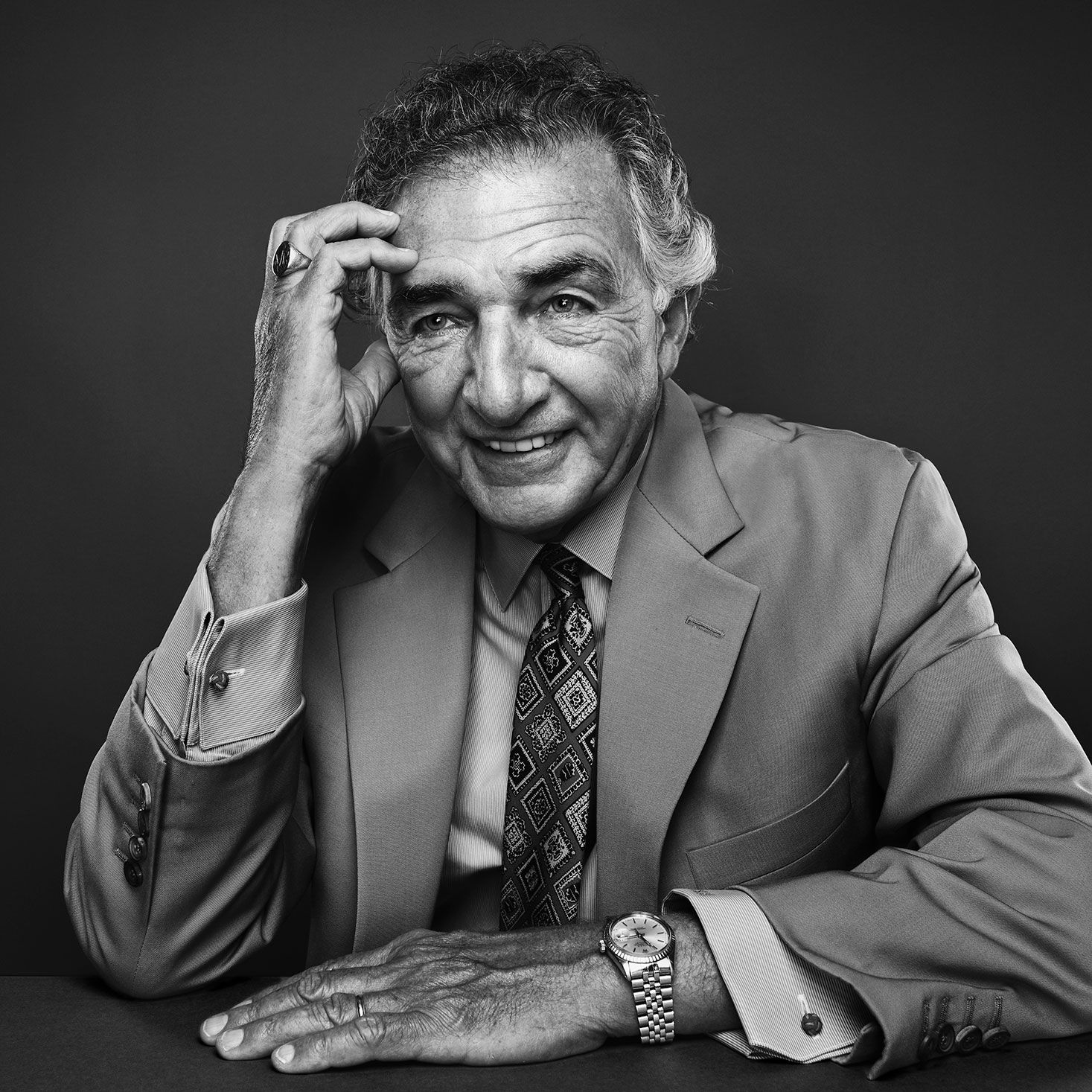 Elderly man in suit smiling in black and white portrait.