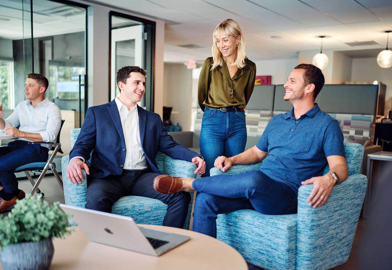 Three professionals having a casual meeting in a modern office lounge, smiling and engaged in conversation.