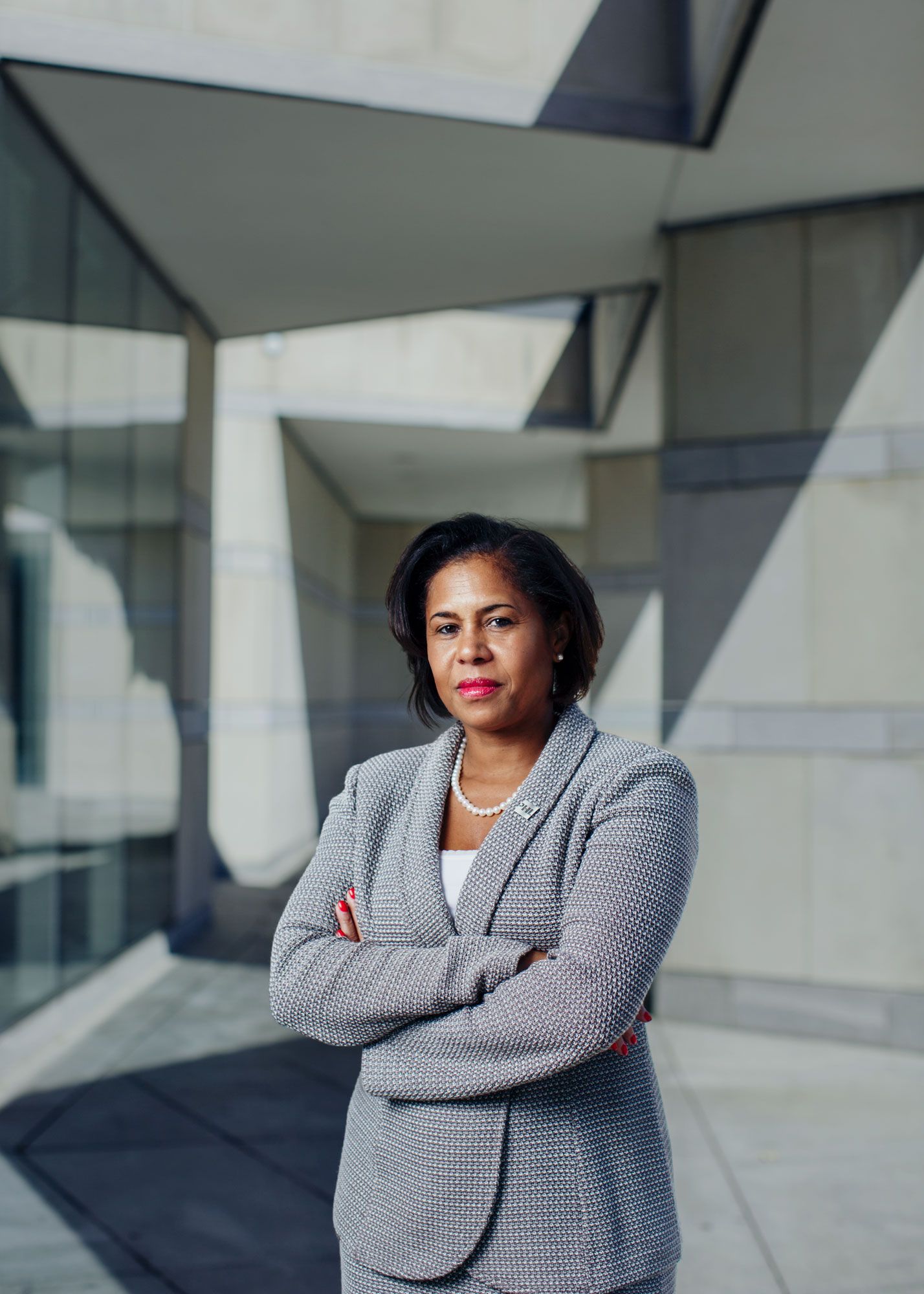 Confident businesswoman in gray suit standing with arms crossed outside modern building.