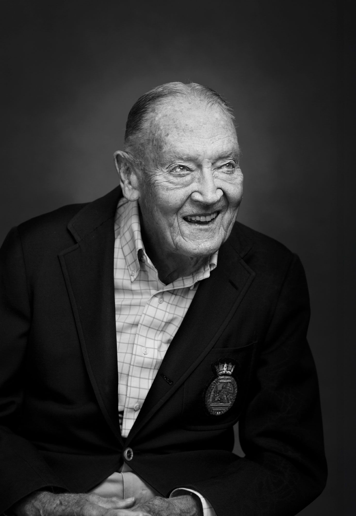 Elderly man in black blazer with medal laughing warmly in black and white portrait photo.