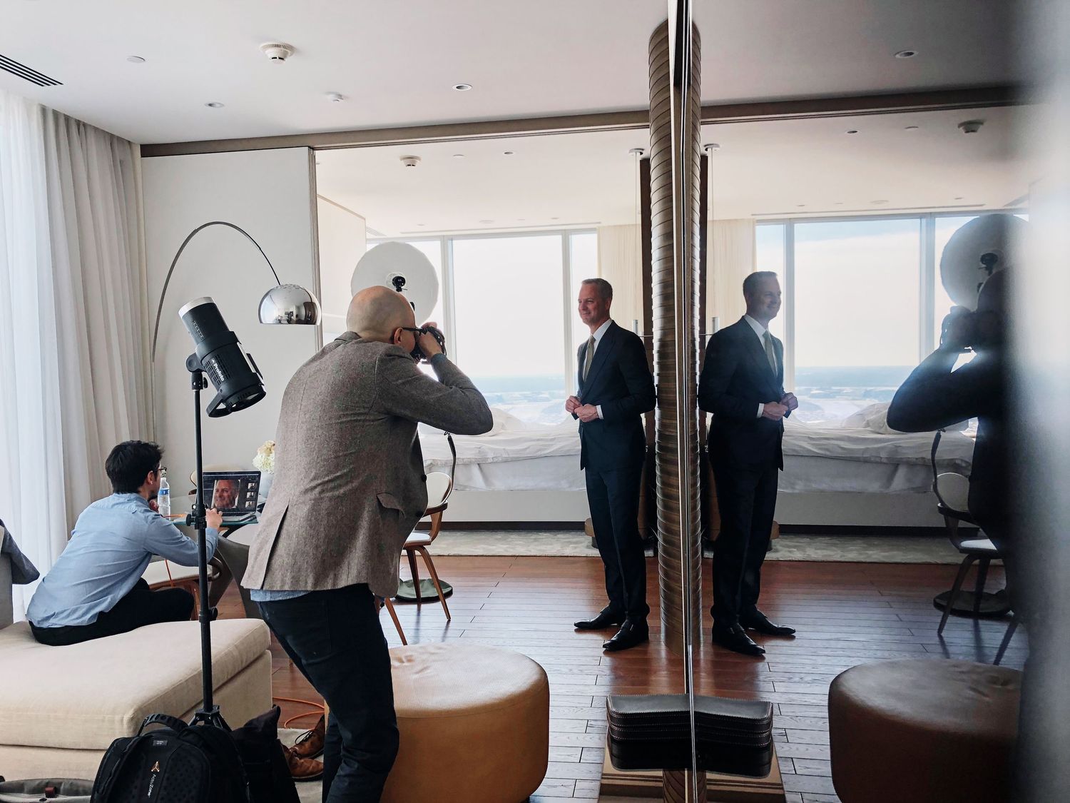 Photographer capturing two men in suits during an indoor photo shoot in a modern hotel room.