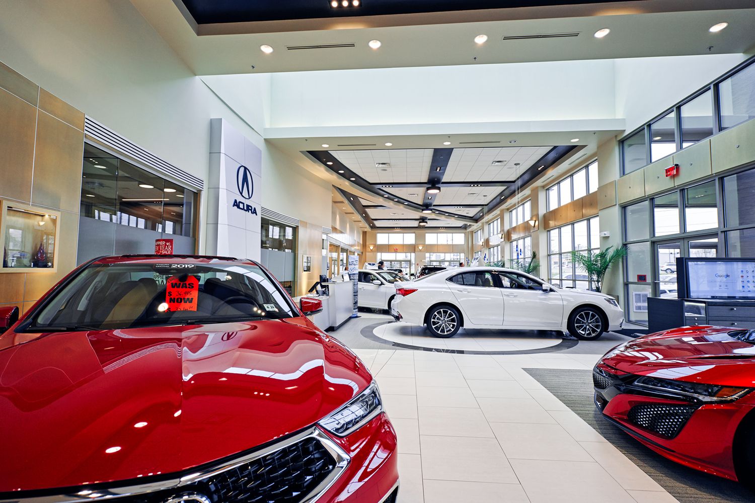 Acura dealership showroom featuring red and white luxury vehicles displayed on a polished floor under bright lighting.