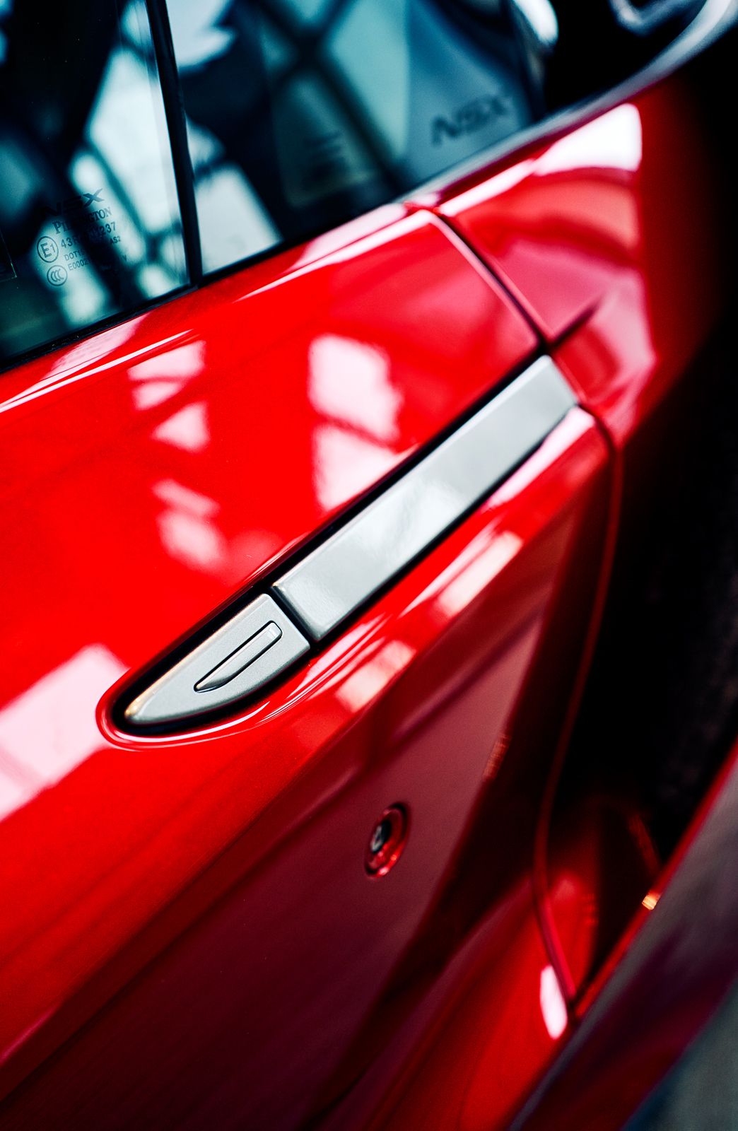 Close-up of a shiny red Acura NSX sports car door handle with chrome accent detail.
