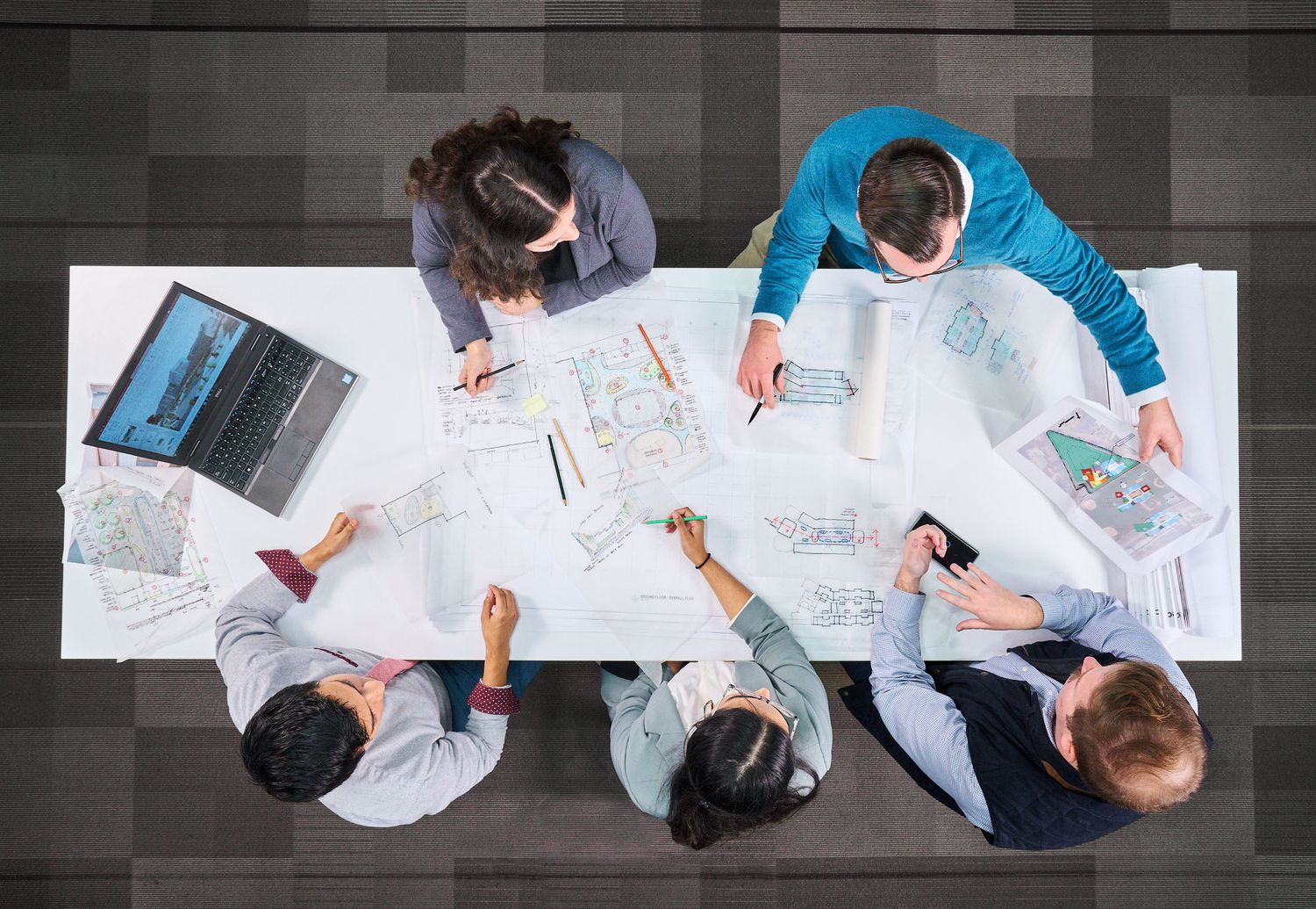 Aerial view of business team collaborating over architectural blueprints and maps on a white conference table.