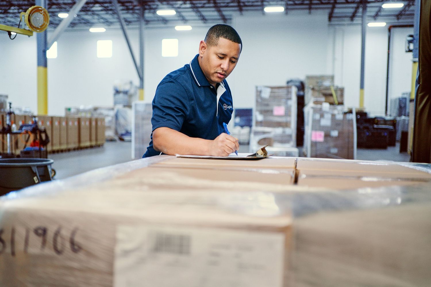 Warehouse worker inspecting and documenting inventory on a clipboard in a distribution center.