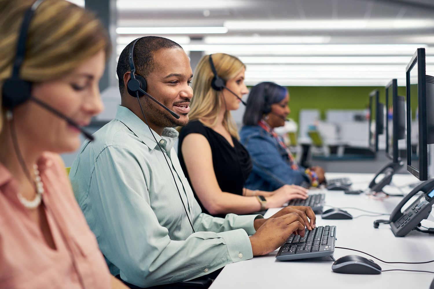 Diverse call center team wearing headsets working at computers in a modern open office environment.