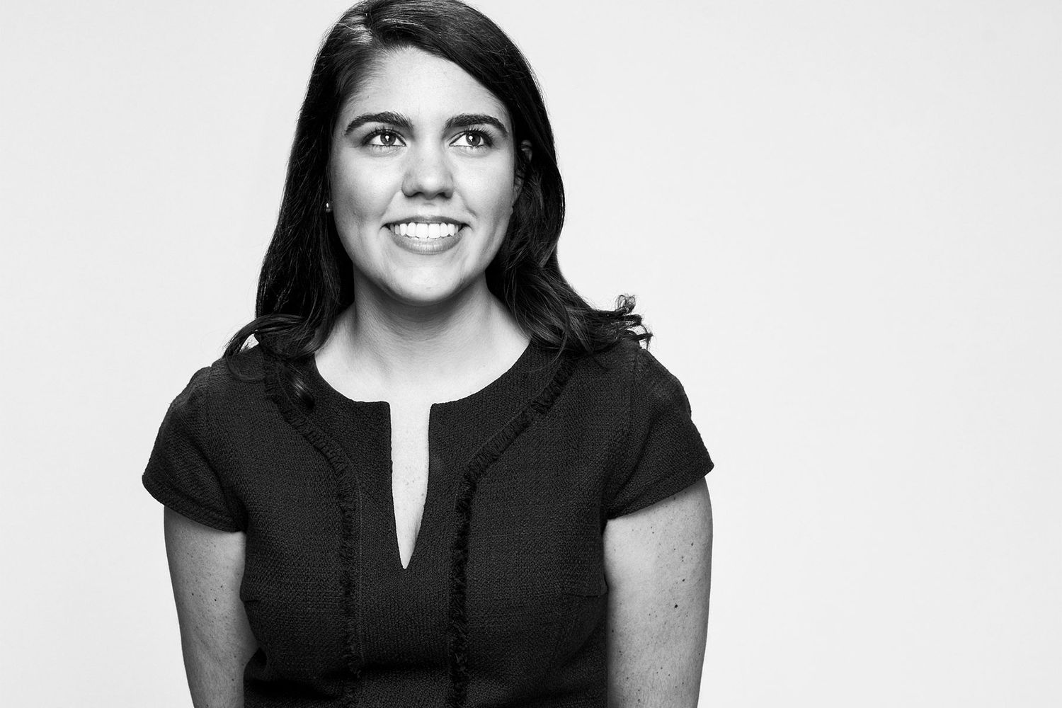 Black and white portrait of smiling woman in dark top against light background.