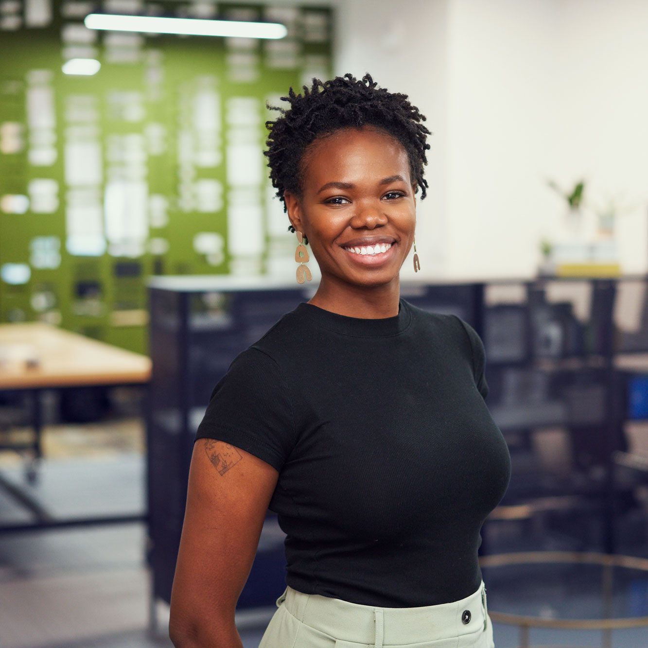 Smiling young Black woman in a black t-shirt standing in a modern creative office workspace.
