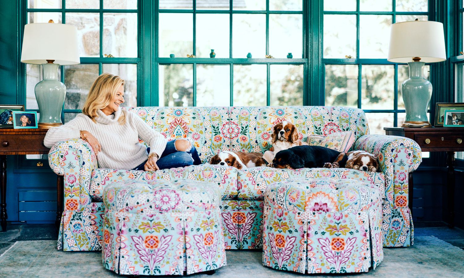 Woman relaxing on colorful floral sofa with two Cavalier King Charles Spaniels.