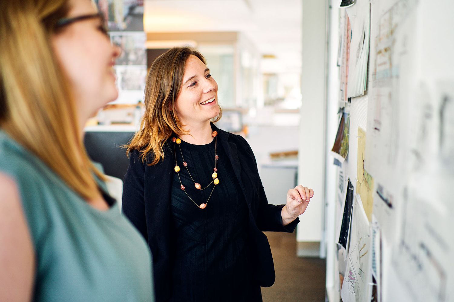 Woman presents design sketches on a board to a colleague in a bright creative office workspace.