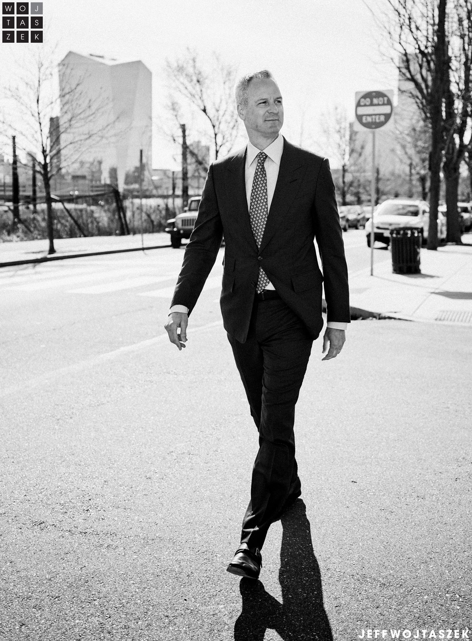 Man in dark suit and tie walking confidently on a city street in black and white photography.
