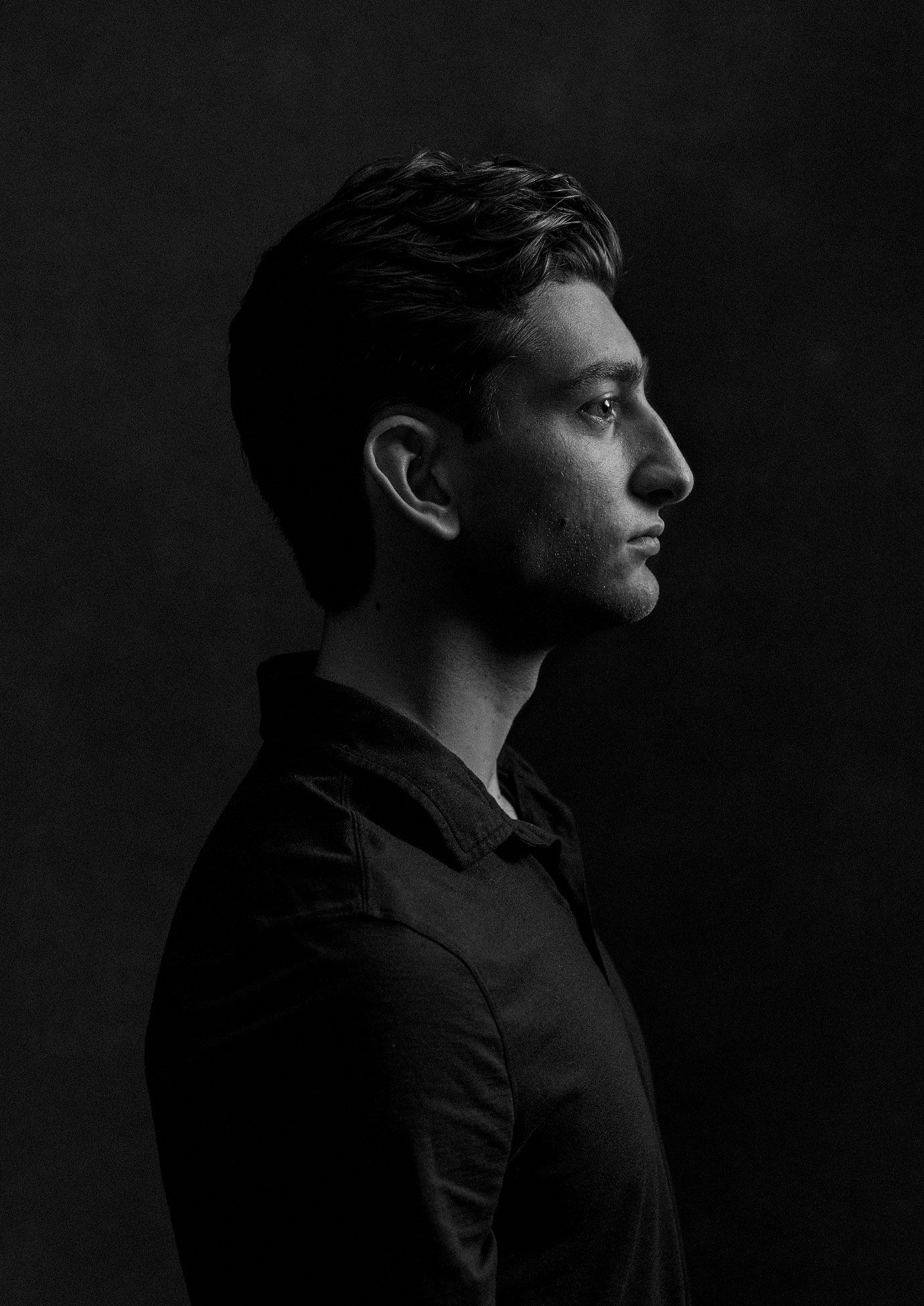 Dramatic black and white side profile portrait of young man against dark background.