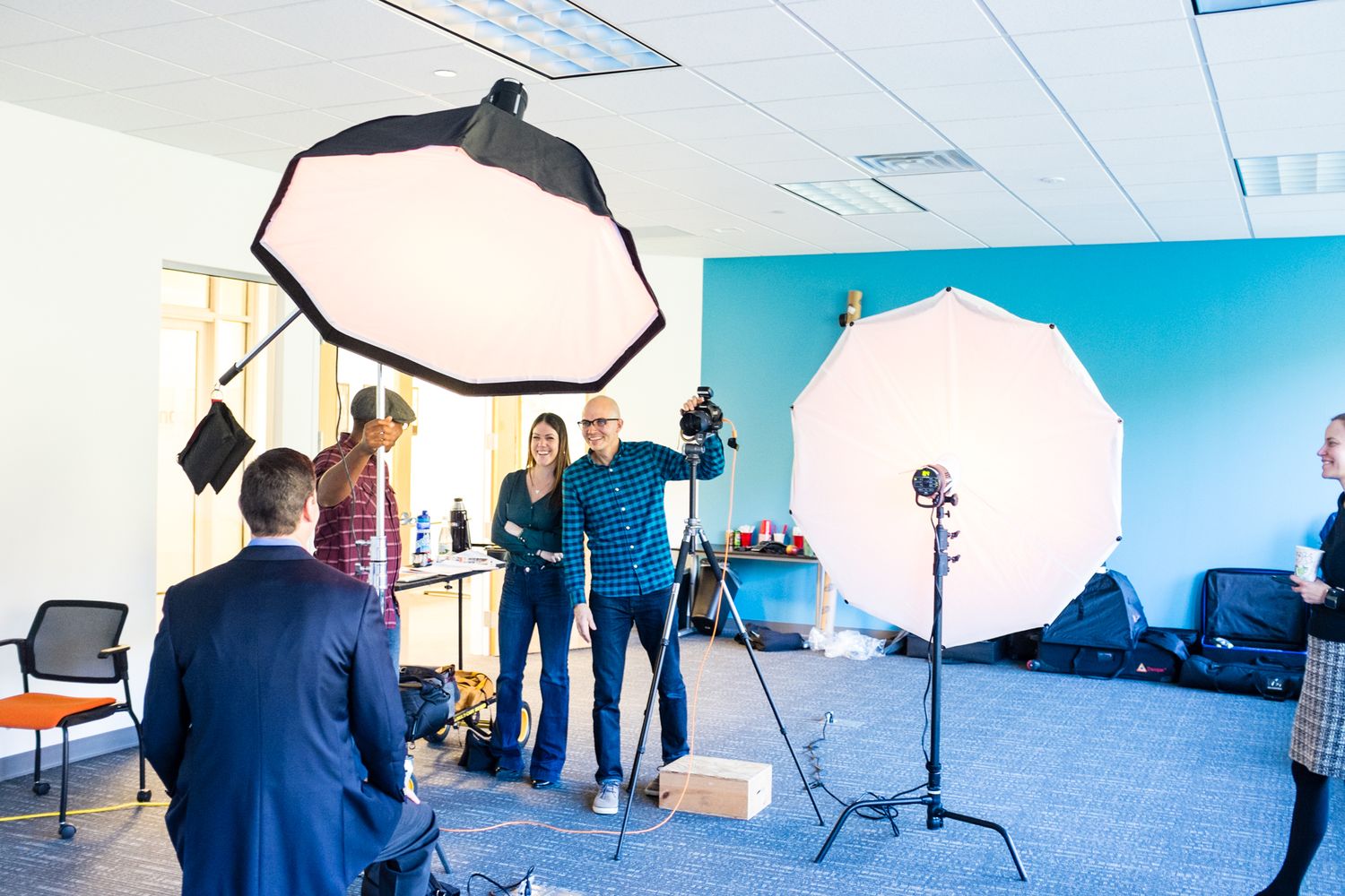 Professional photo shoot setup with studio lights, softboxes, and photographers posing in a modern office space.