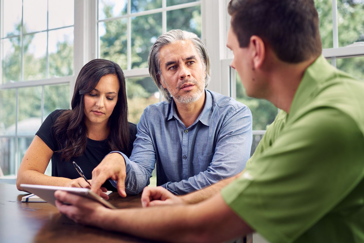 Couple reviewing documents with consultant at wooden table in bright windowed meeting room.