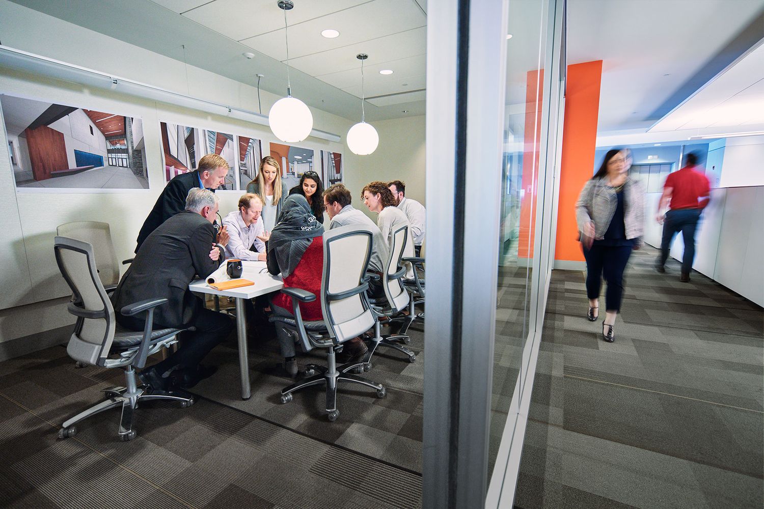 Group of colleagues collaborating in a glass-walled conference room in a modern corporate office.