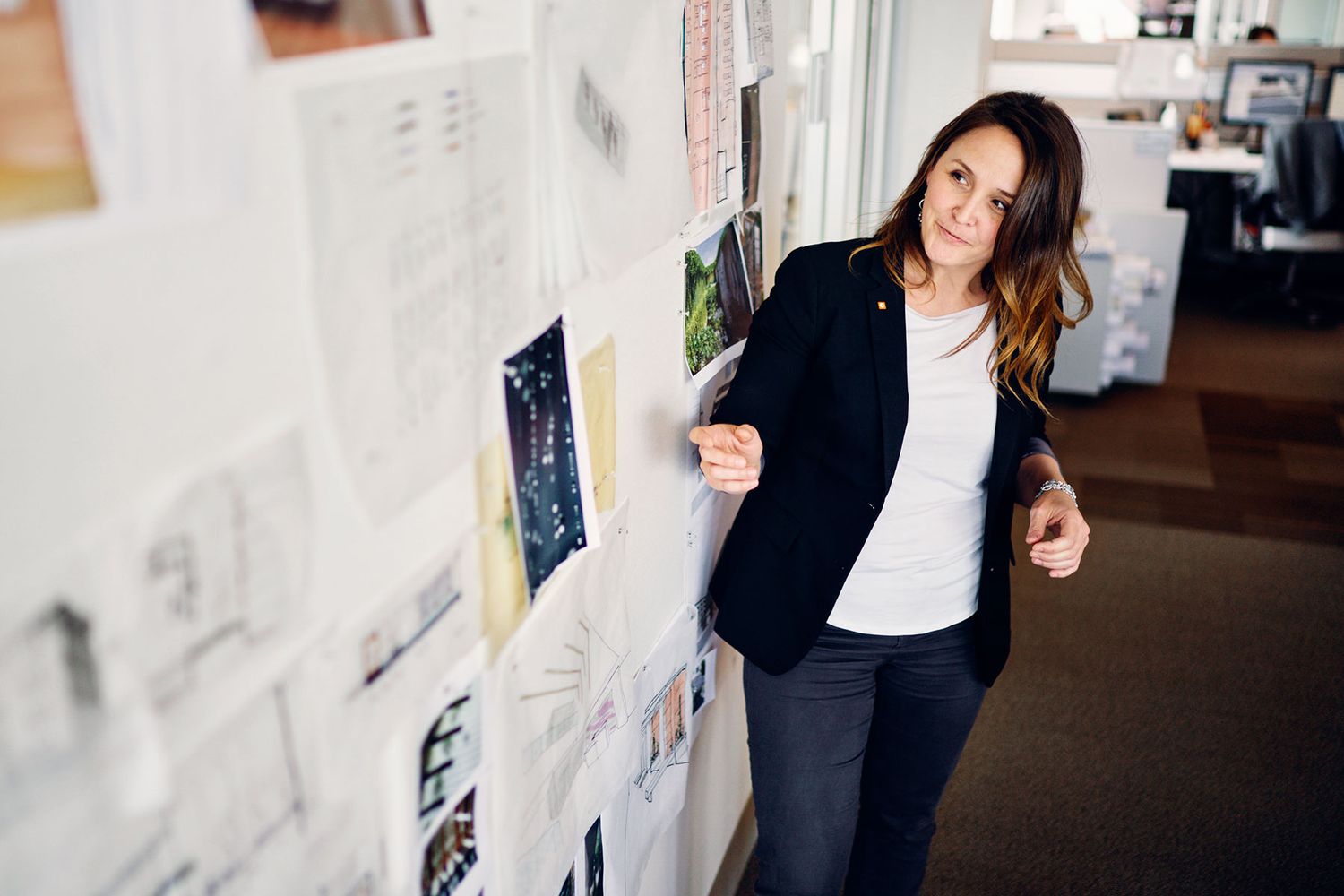 Confident businesswoman in black blazer standing beside a creative mood board in a modern office.