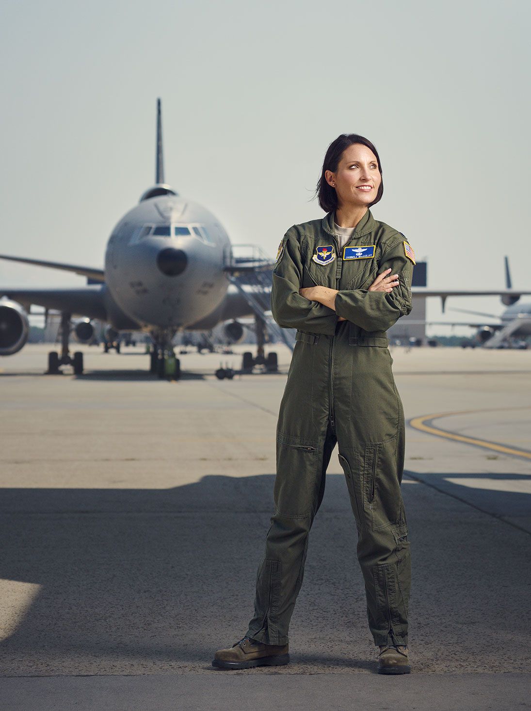 Female pilot in flight suit standing confidently on airport tarmac.