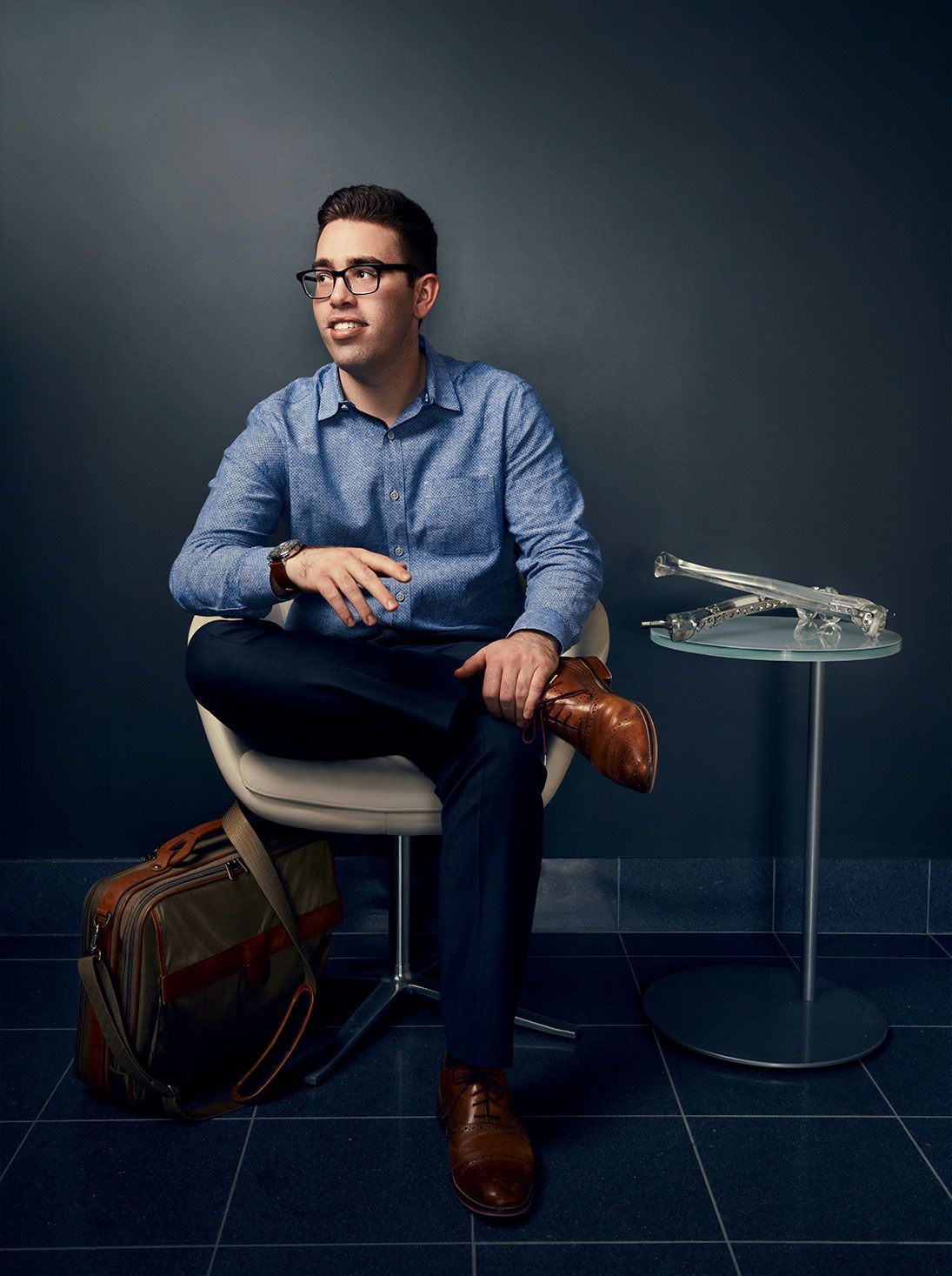 Young man in glasses sitting in modern chair with bag.