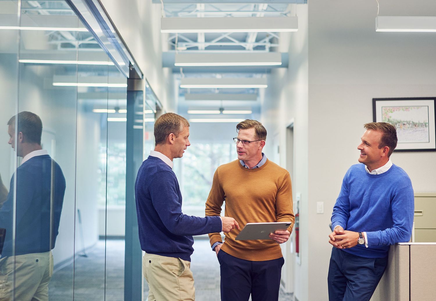 Three businessmen having an informal discussion in a bright modern office hallway.