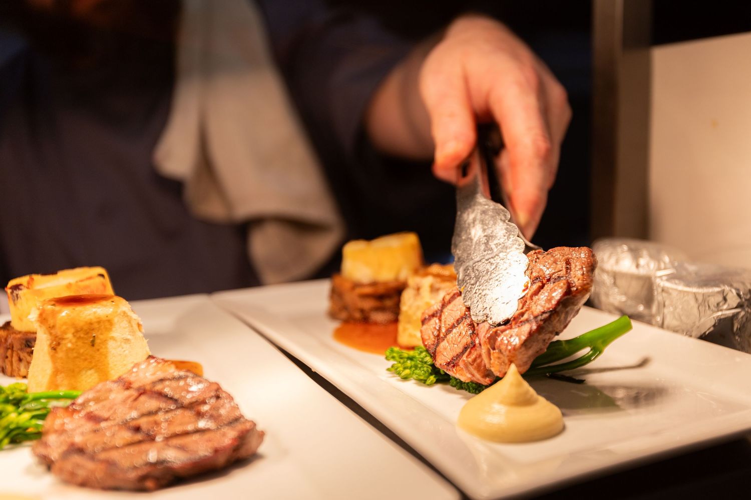 Chef plating a gourmet steak dish with roasted potatoes and asparagus.