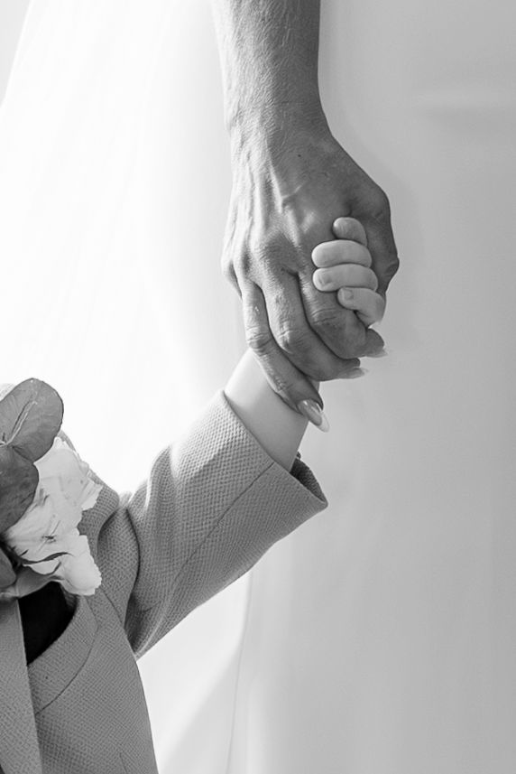 Black and white photo of a couple holding hands, bride in white dress and groom in suit at a wedding ceremony.