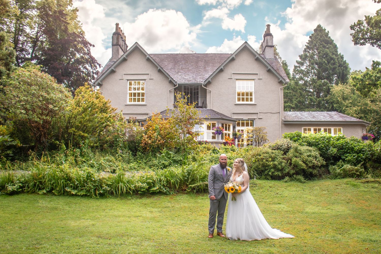 Bride and groom posing in front of a charming country house surrounded by lush gardens.