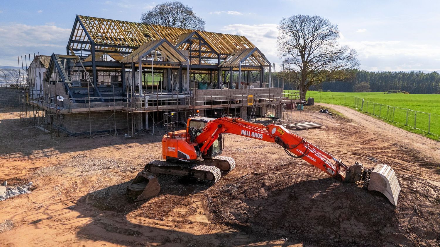 Orange excavator at a residential construction site with steel frame structure being built outdoors.