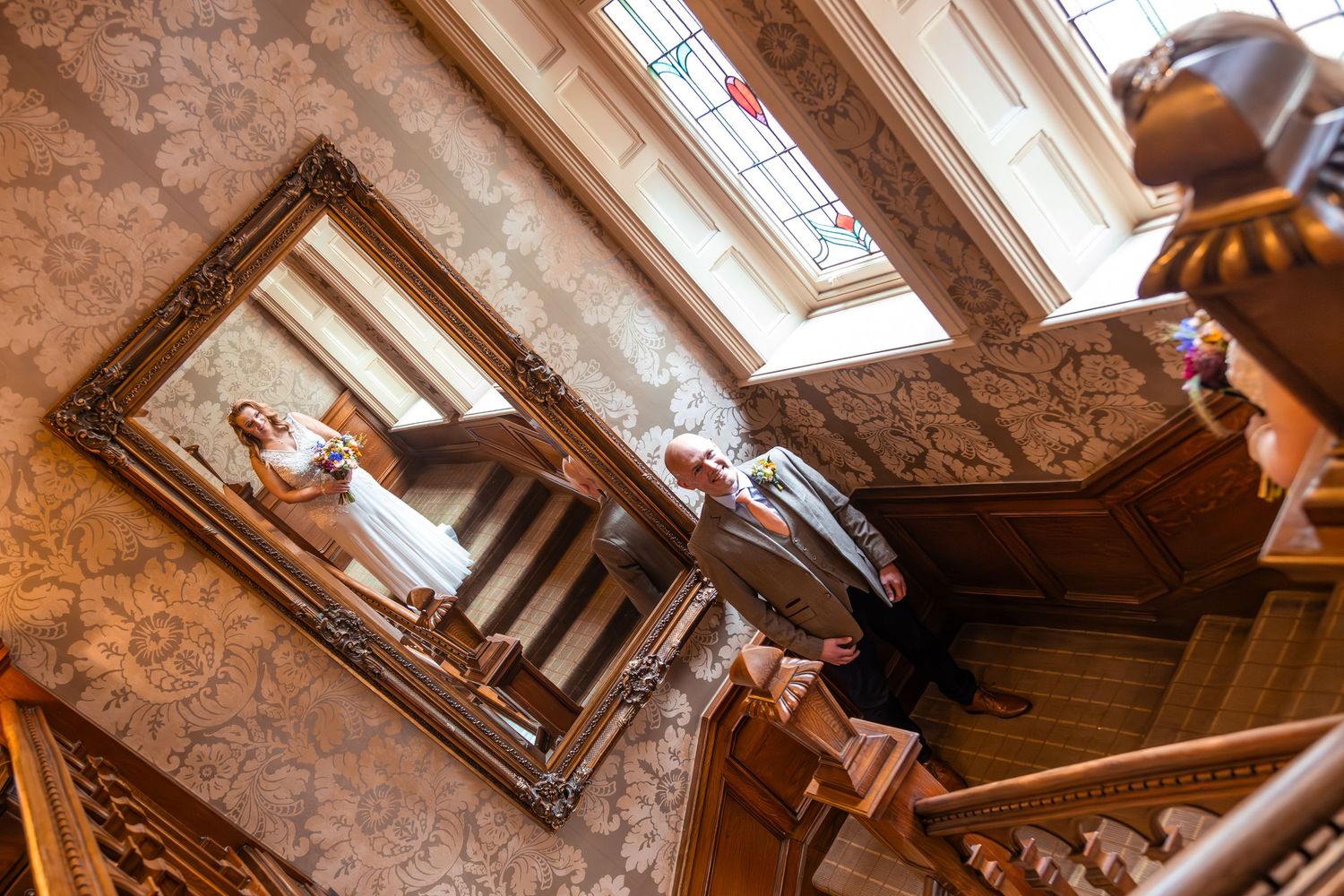 Bride and groom reflected in ornate mirror on grand staircase.