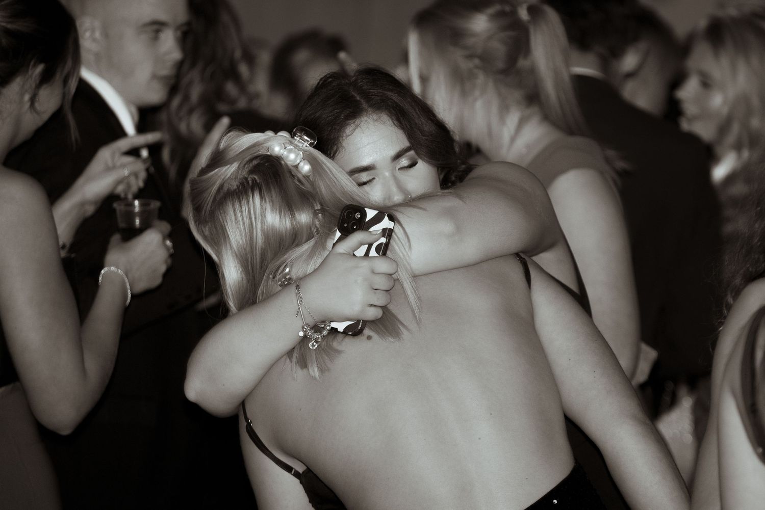 Black and white photo of two women sharing a warm hug on a formal event dance floor.