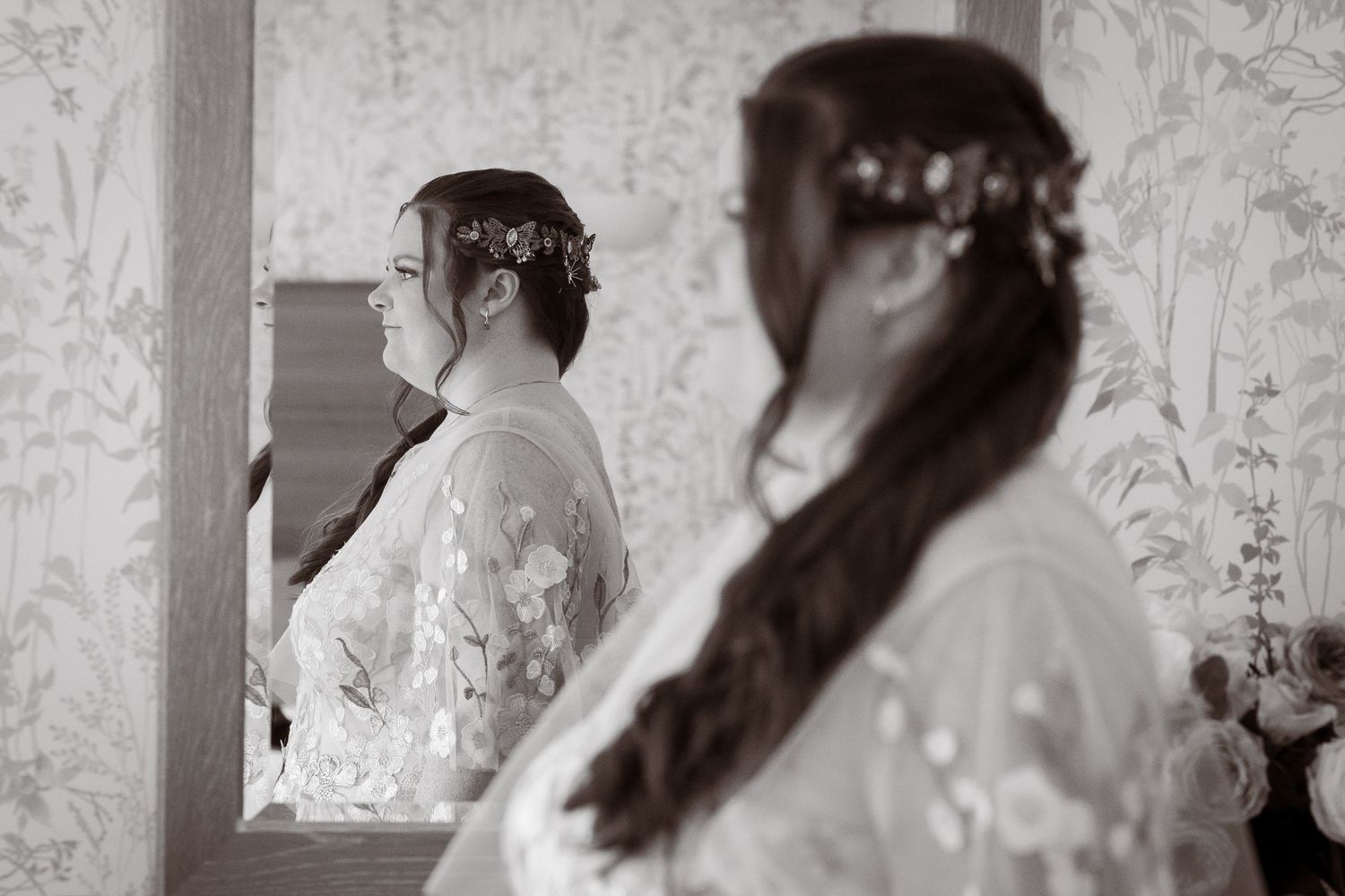 Black and white portrait of a bride in lace robe reflected in a mirror before wedding.