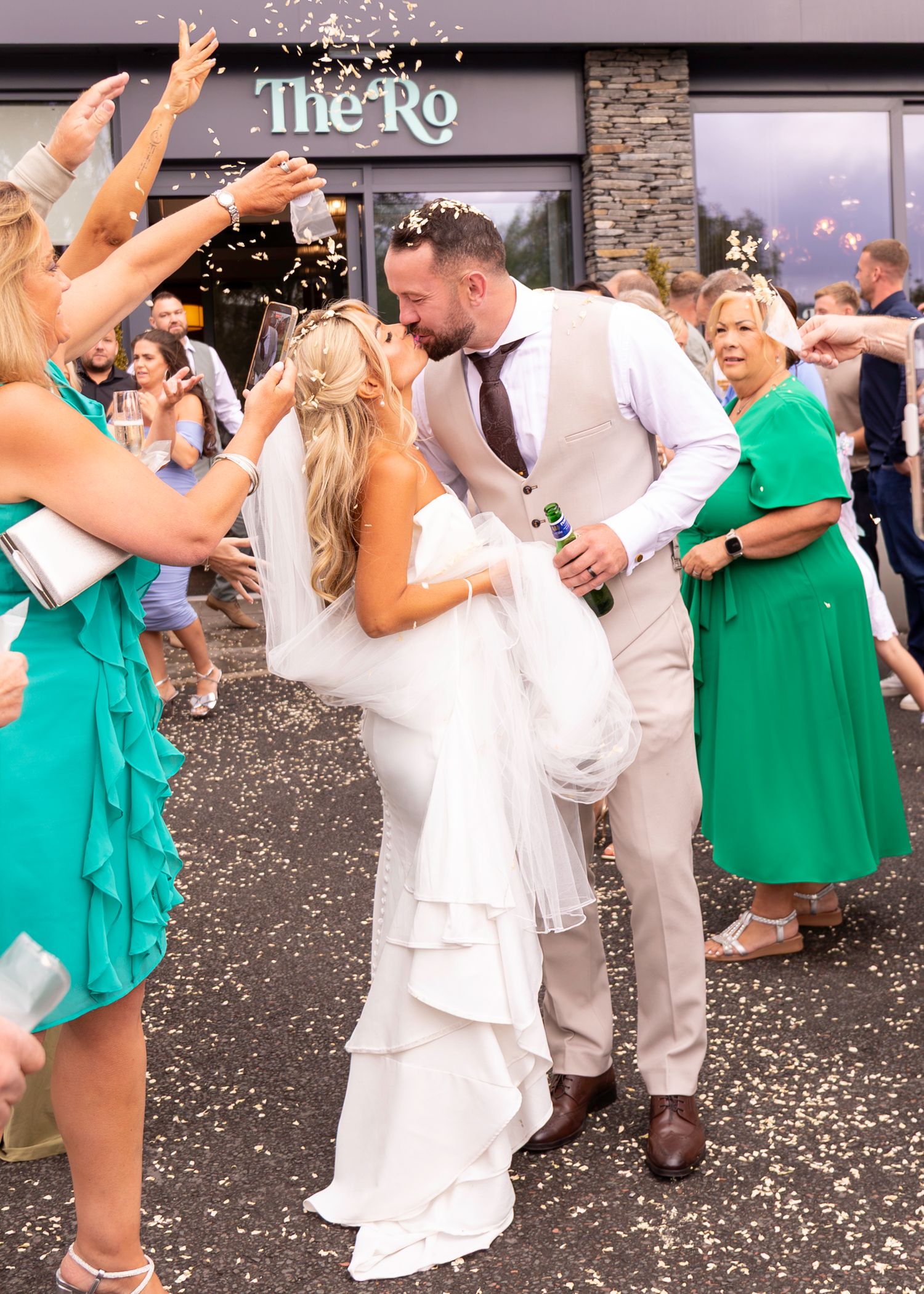 Bride and groom share a kiss outside The Ro venue while guests throw confetti and hold sparklers at their wedding celebration.