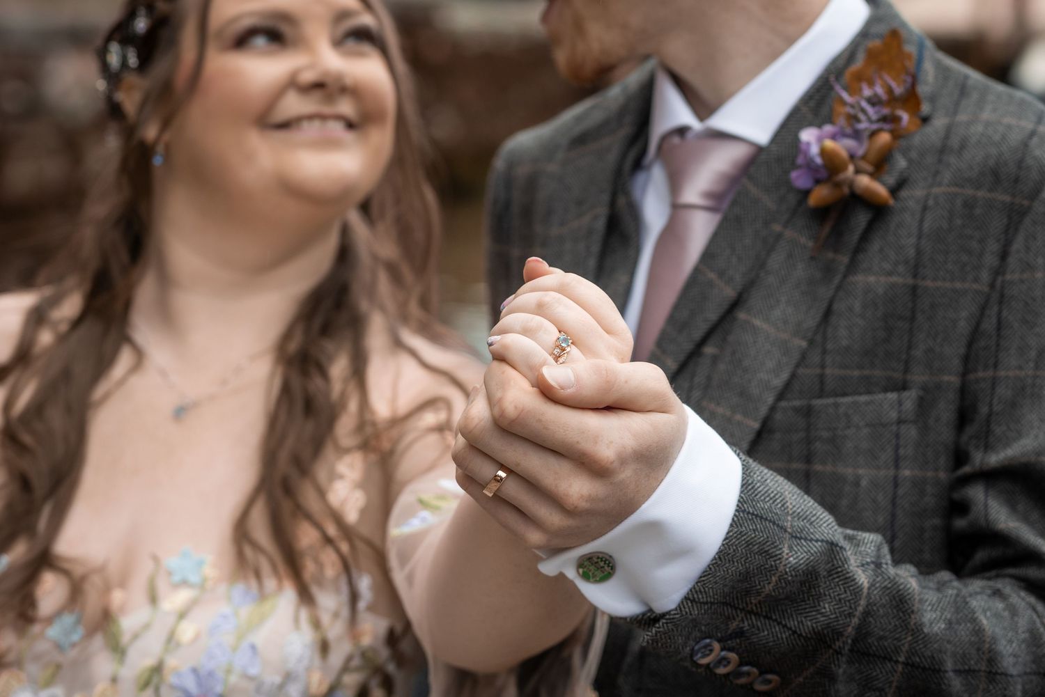 Close-up of bride and groom holding hands showing wedding ring during outdoor ceremony.
