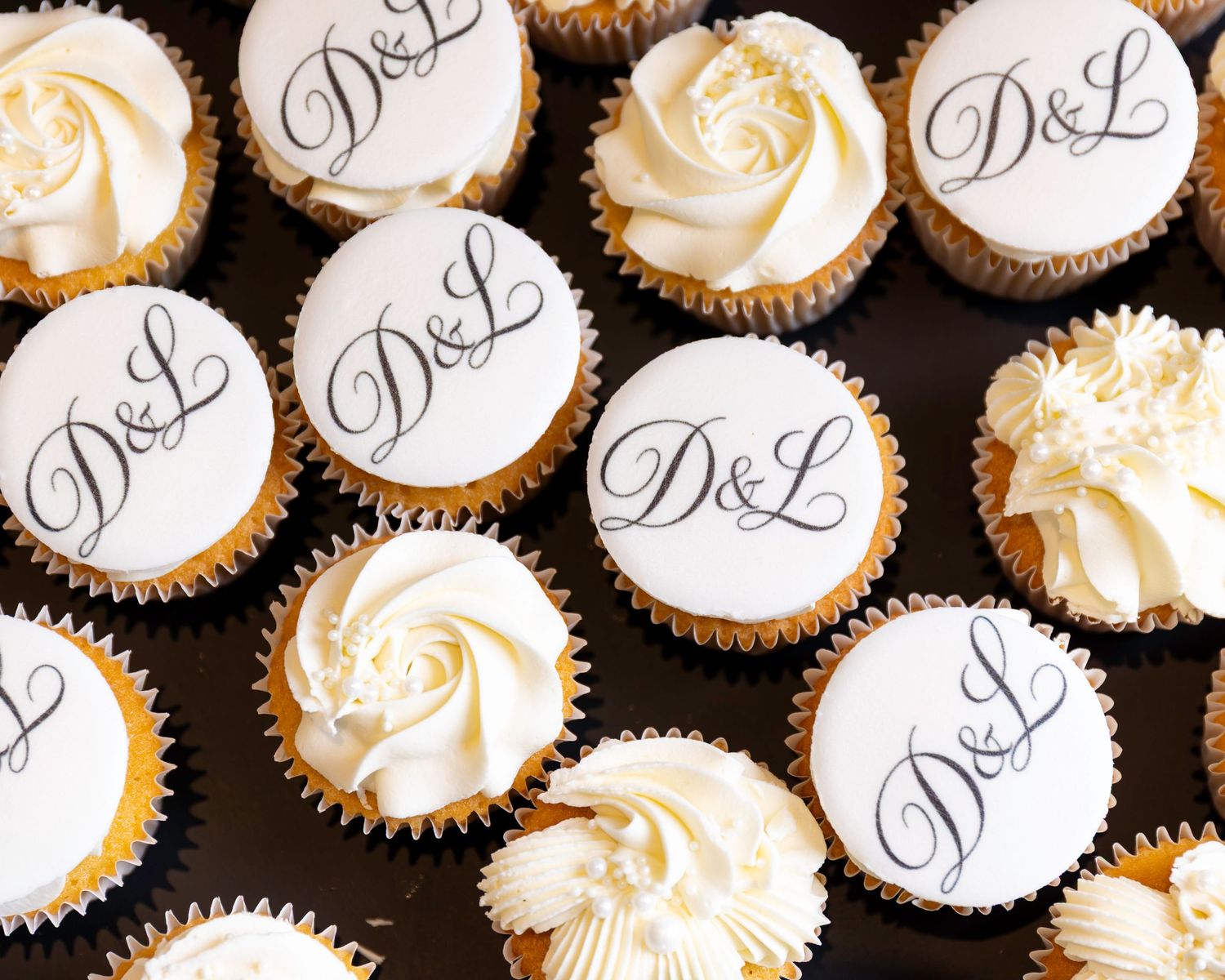 Wedding cupcakes with D&L monogram and white frosting on display.