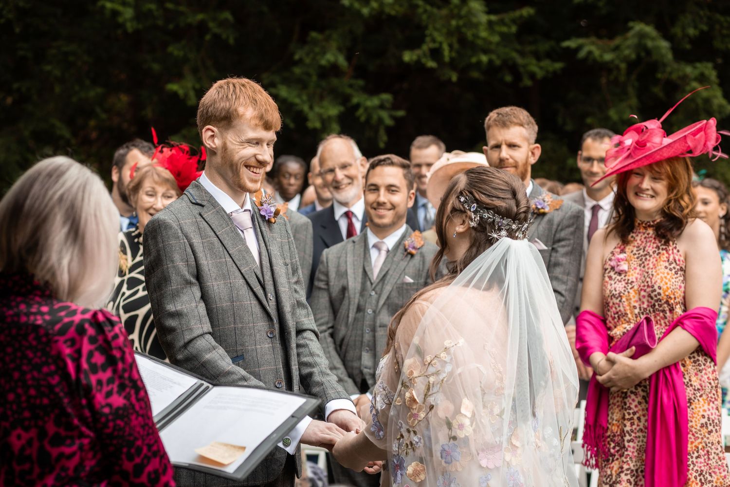 Groom smiling as bride lifts her veil during an outdoor garden wedding ceremony.