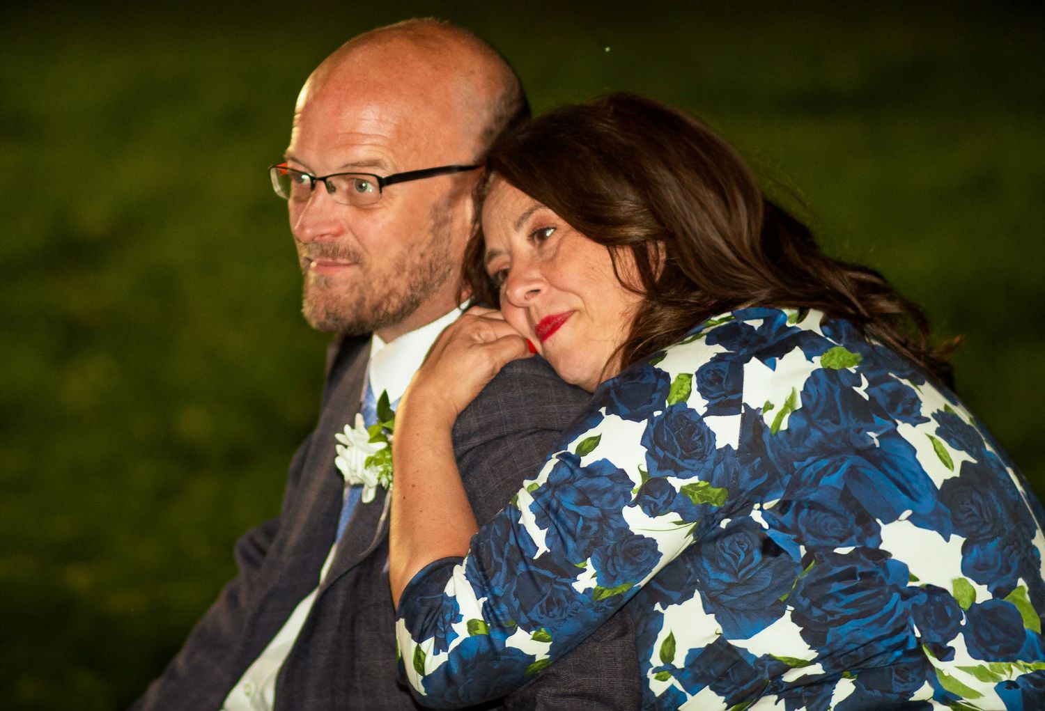 A couple shares a tender moment at an outdoor wedding reception, woman resting her head on mans shoulder.