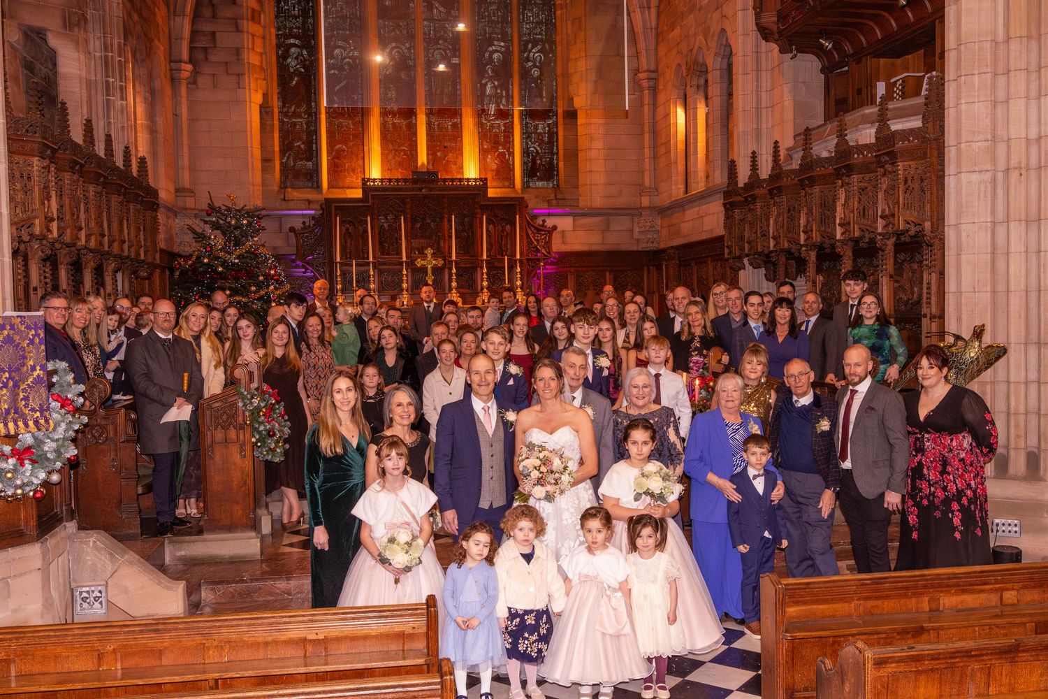 Large wedding party group photo inside a stunning historic church with warm golden lighting.
