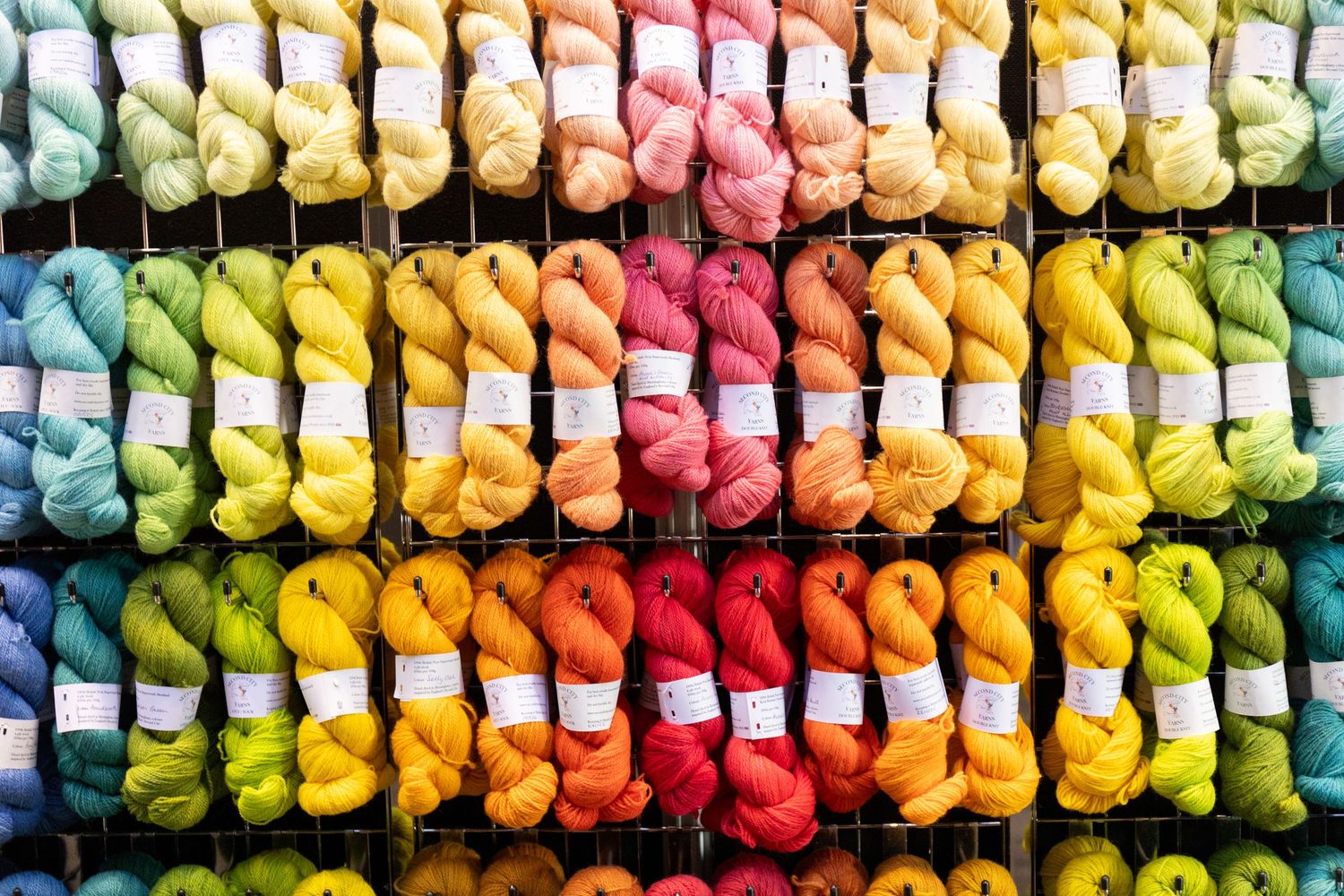 Rows of vibrant rainbow-colored yarn skeins neatly arranged on a display rack.