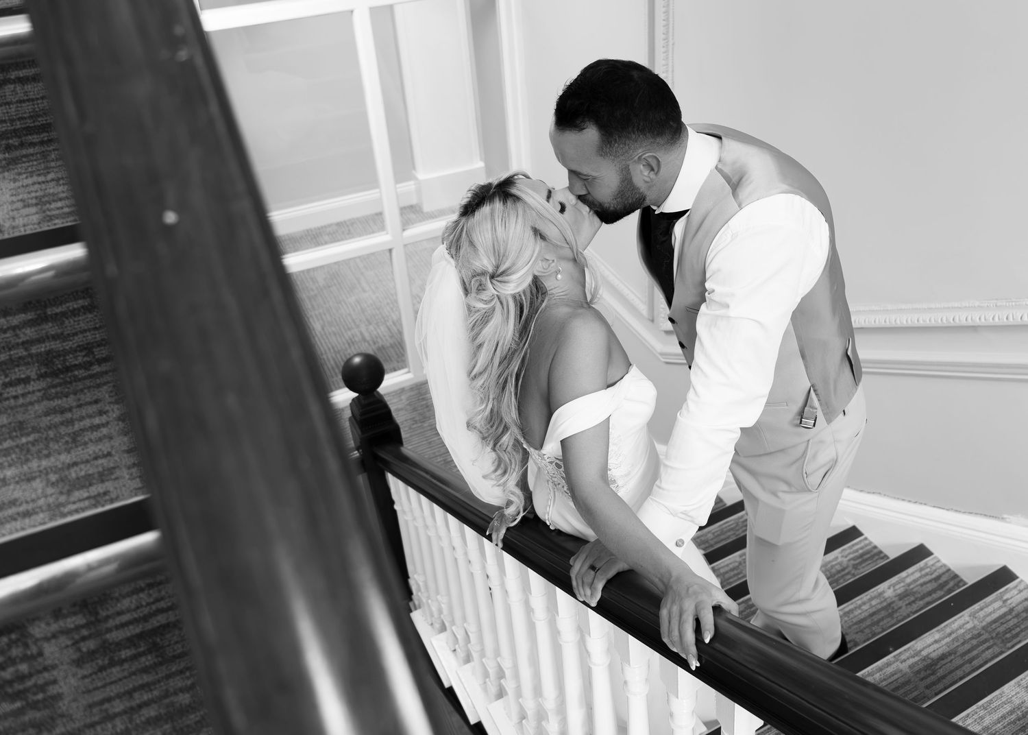 Black and white photo of a bride and groom sharing a romantic kiss on a staircase at their wedding.