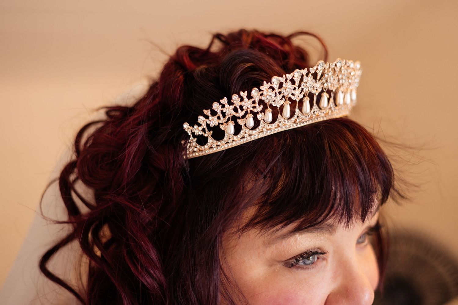 A bride wearing an elegant rose gold crystal tiara in her curly dark red hair on her wedding day.